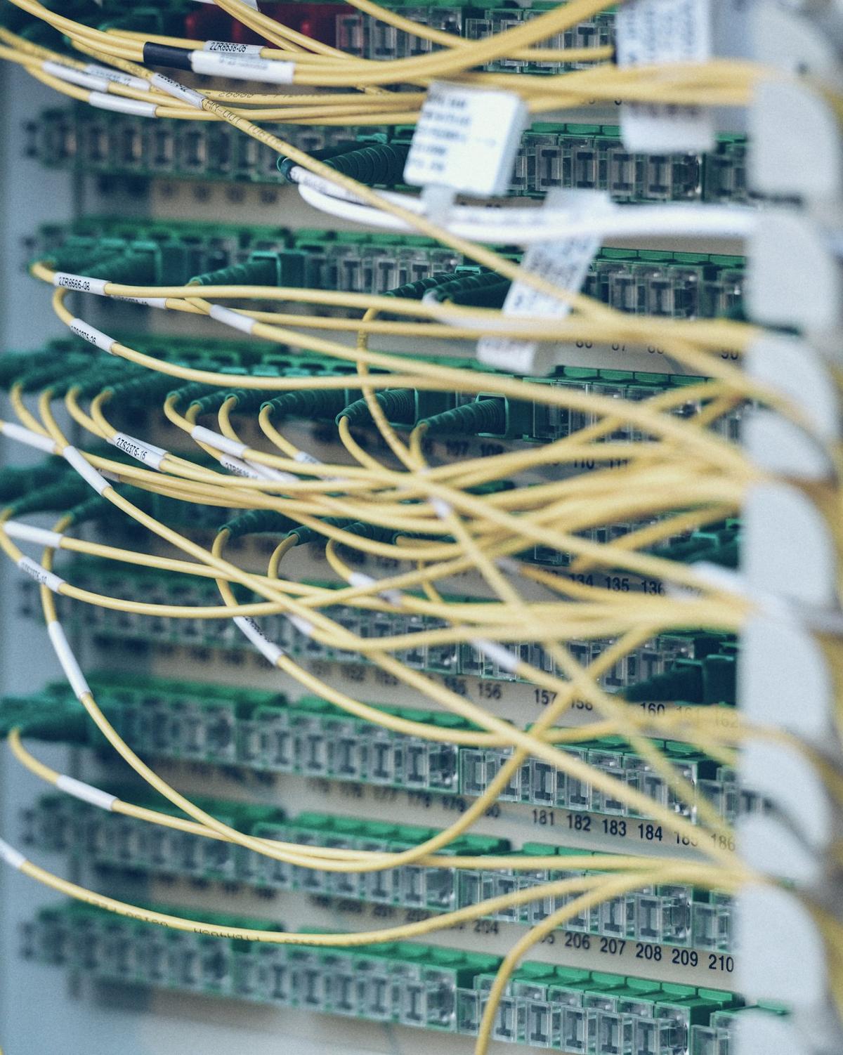 Des fibres optiques jaunes raccordées une à une sur un panneau de brassage.