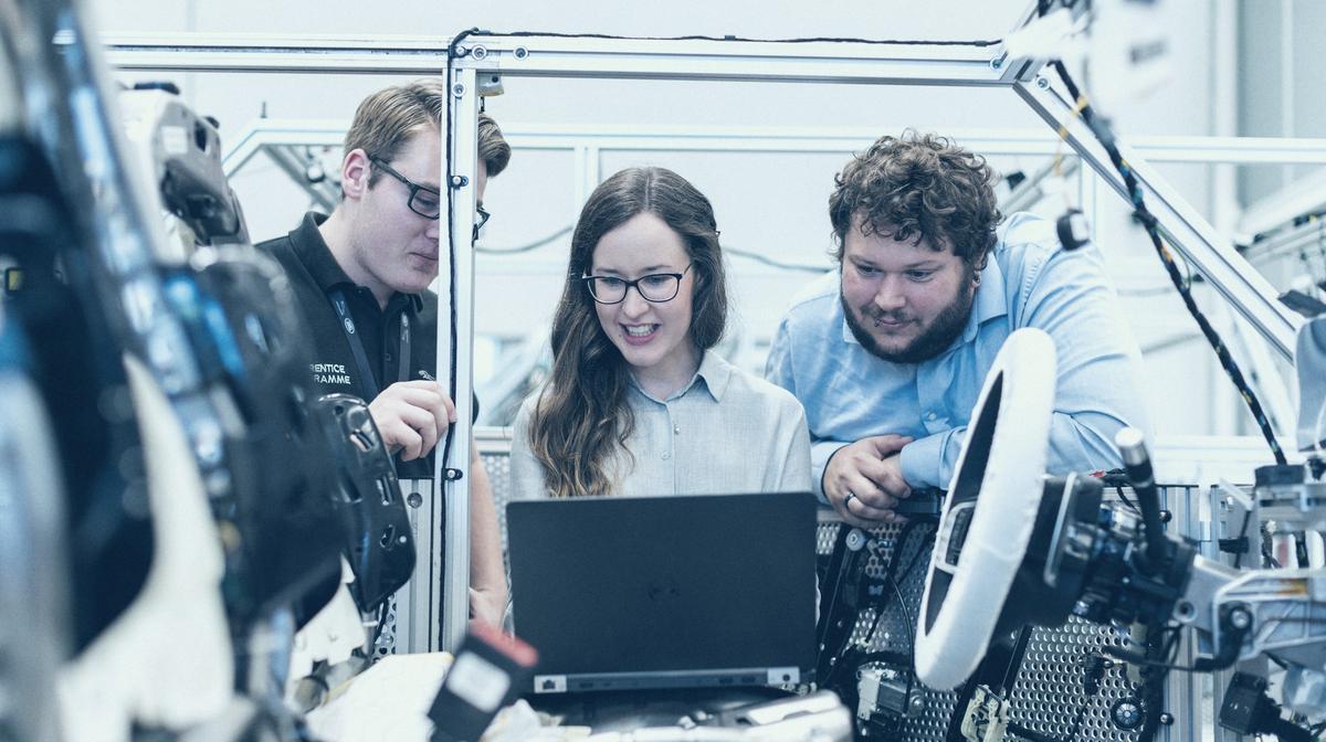 Trois ingénieurs penchés sur un ordinateur portable, au milieu d'un banc d'essai en atelier.