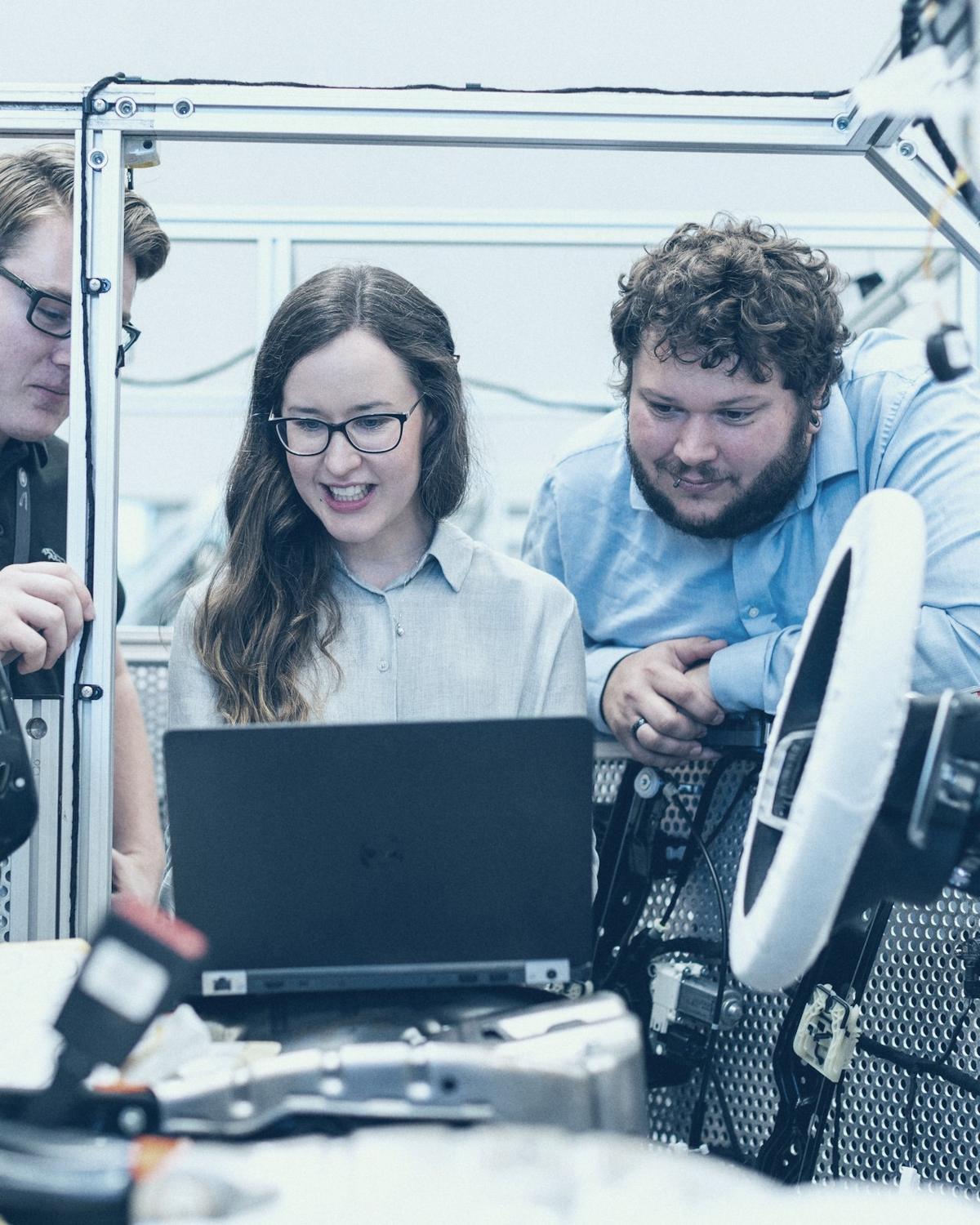 Trois ingénieurs penchés sur un ordinateur portable, au milieu d'un banc d'essai en atelier.