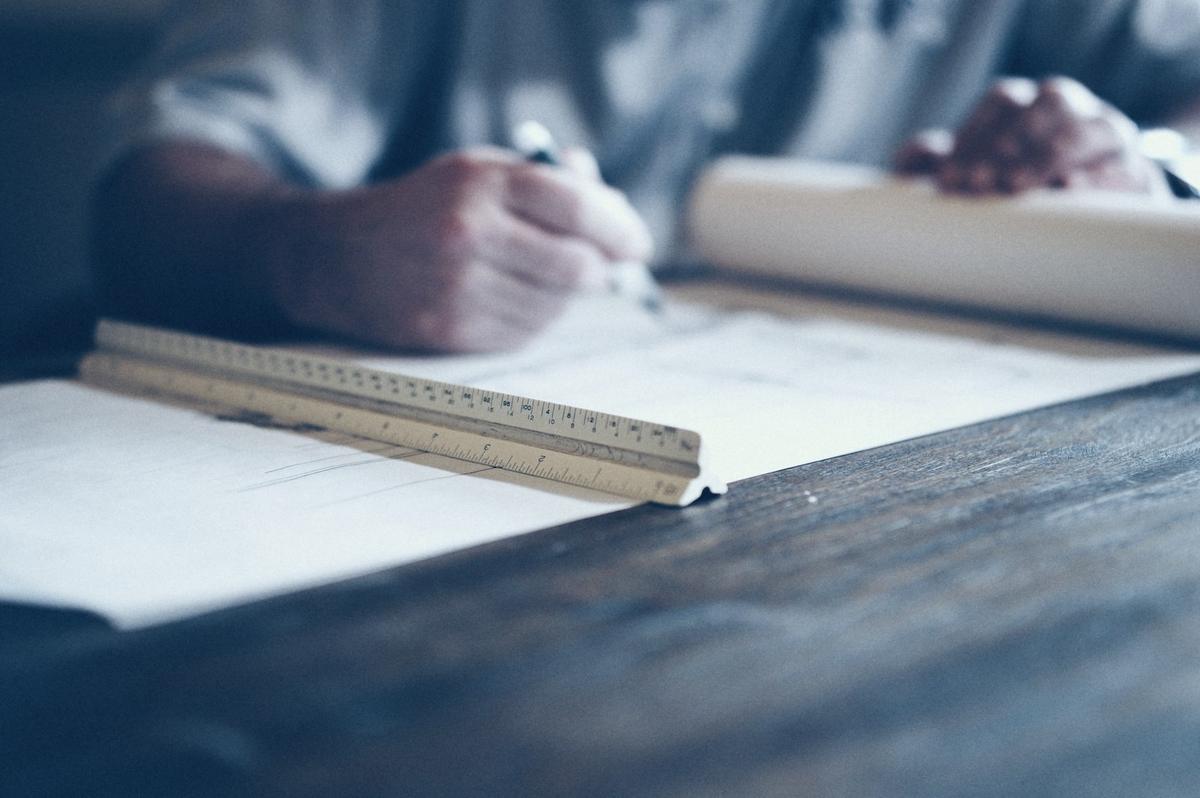 A hand drawing a plan with a ruler on a large sheet of paper.